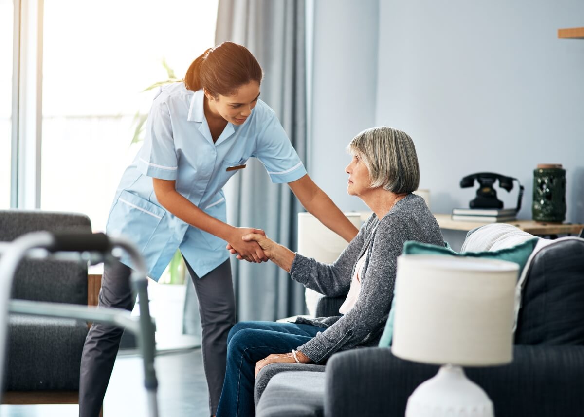 a picture of an elderly woman on the couch at a long-term care facility and a nurse grabbing her hand to help her up