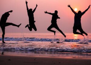 a silhouette of 4 people on the beach at sunset jumping