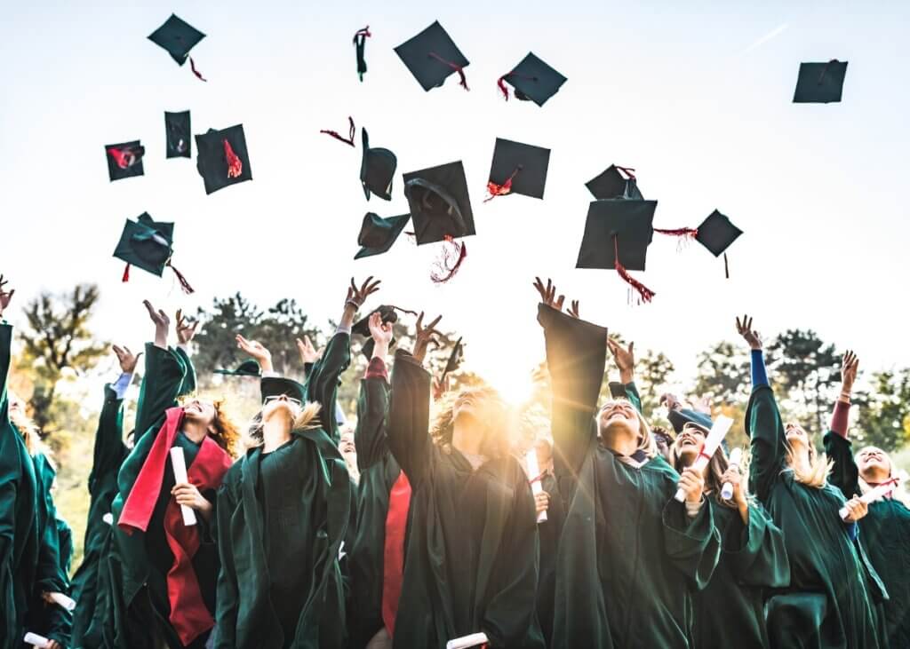 a group of young adults or high schoolers at their graduation throwing up their caps in the air