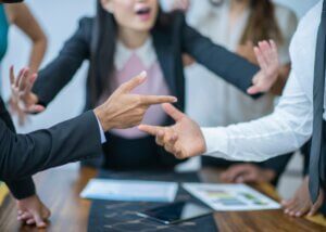 a picture of two hands pointing at each other like they are in an argument and then a lady in the back trying to diffuse the argument.