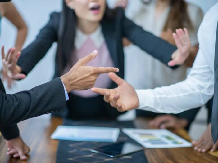 a picture of two hands pointing at each other like they are in an argument and then a lady in the back trying to diffuse the argument.