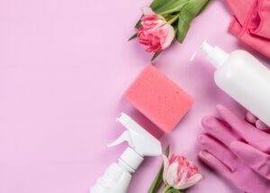 a pink background with cleaning supplies. there is a pink and spring theme. some gloves, cleaning bottles, and flowers