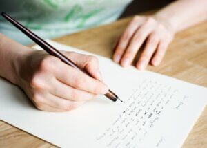 an overhead picture of a person writing a letter. you can see a picture of the paper and the pen and then the individuals hands.