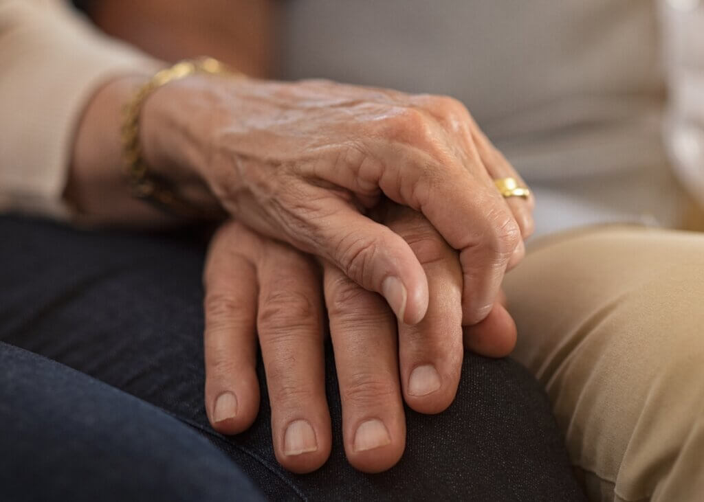 aging seniors holding hands. just a shot of their hands on the older womans thigh and they are holding each others.