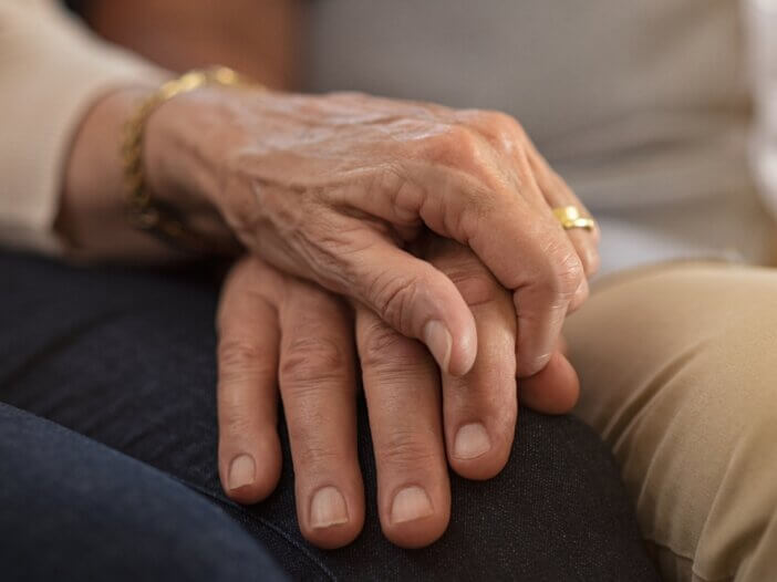 aging seniors holding hands. just a shot of their hands on the older womans thigh and they are holding each others.