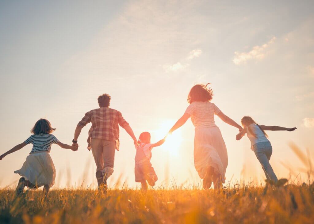 a family holding hands running in a field. there are three children and a mother and a father