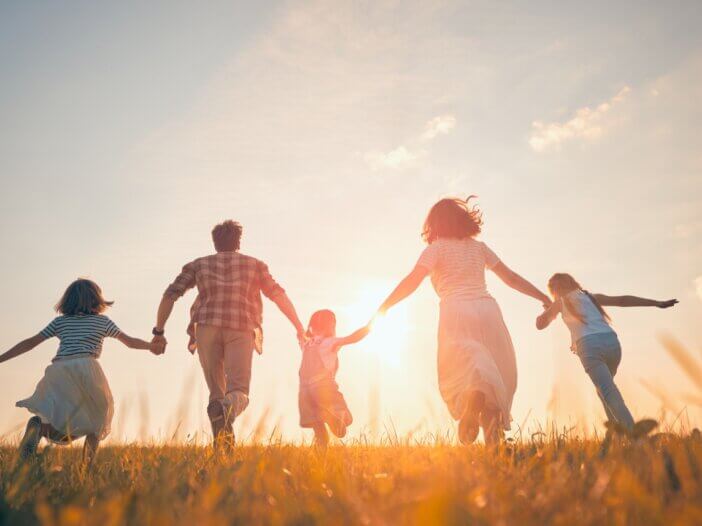 a family holding hands running in a field. there are three children and a mother and a father