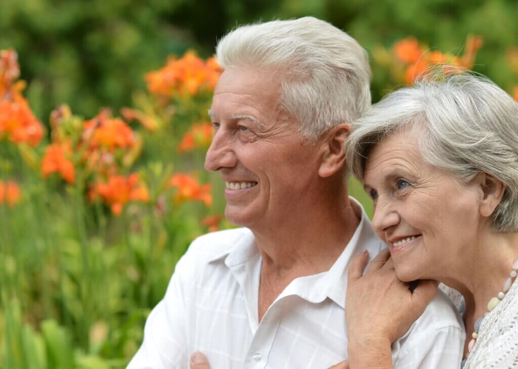two elderly people sitting in a garden smiling