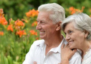 two elderly people sitting in a garden smiling