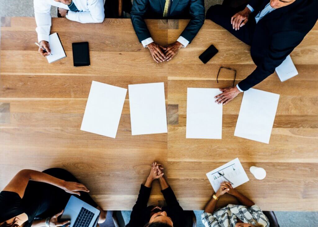 an overhead picture of a table with 6 people at it. three on each side. they are all talking estate planning with documents in the middle of the table that they are looking at.