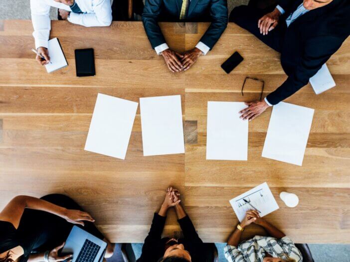 an overhead picture of a table with 6 people at it. three on each side. they are all talking estate planning with documents in the middle of the table that they are looking at.