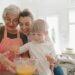 a grandmother and a mother baking with a little boy. they are all close together and smiling and mixing a bowl of ingredients.