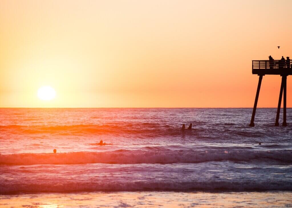a picture of a sunset on the beach and the pier in the back