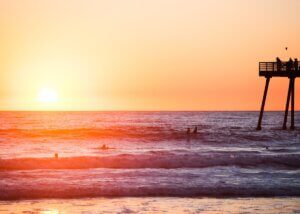 a picture of a sunset on the beach and the pier in the back