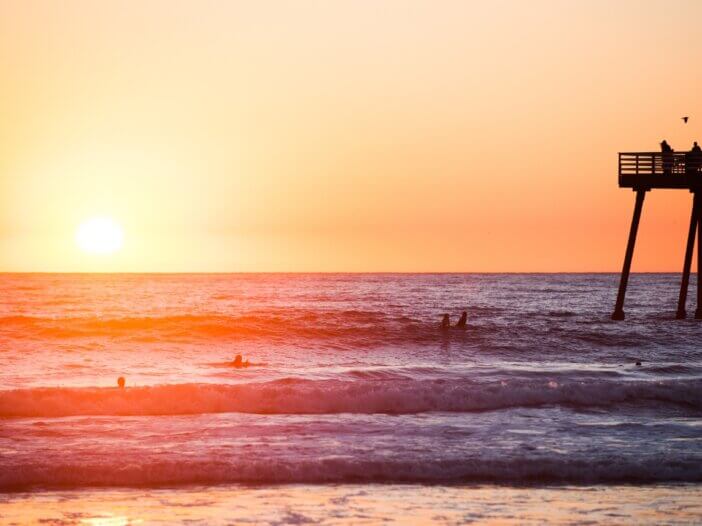 a picture of a sunset on the beach and the pier in the back