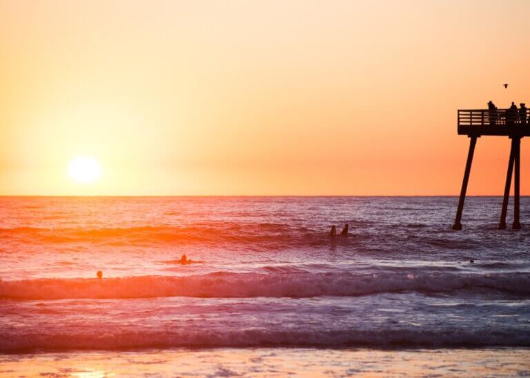 a picture of a sunset on the beach and the pier in the back