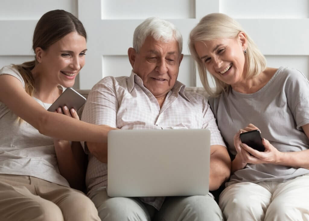 an older dad with his daughter and wife sitting on the couch smiling and looking at their computer