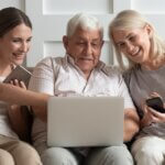 an older dad with his daughter and wife sitting on the couch smiling and looking at their computer
