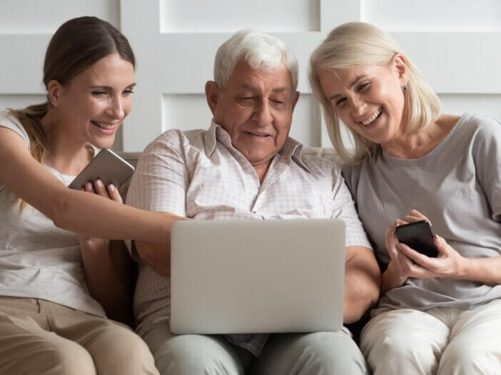an older dad with his daughter and wife sitting on the couch smiling and looking at their computer