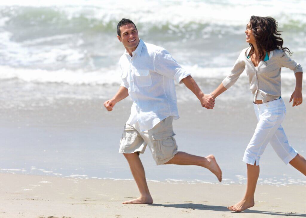 a couple holding hands and running on the beach.