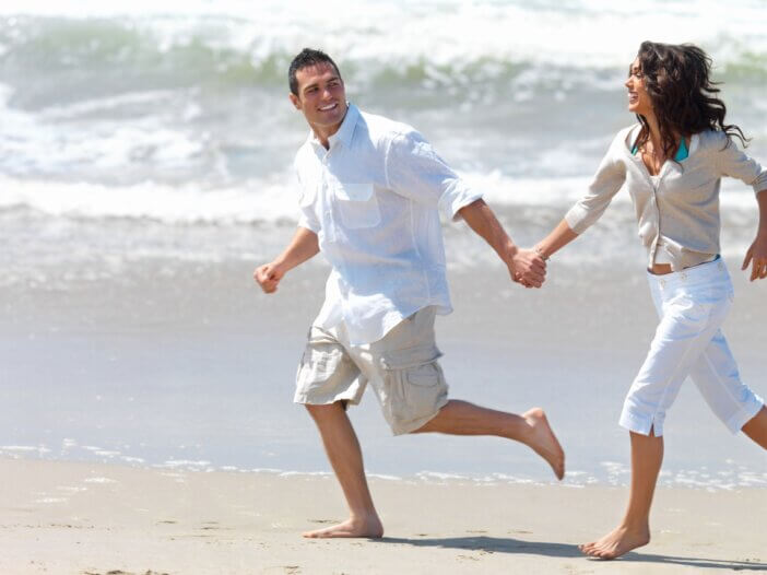 a couple holding hands and running on the beach.