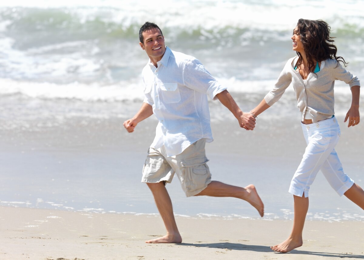 a couple holding hands and running on the beach.