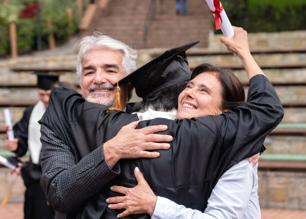 a kid hugging his parents in his graduation cap and gown with his diploma in the air