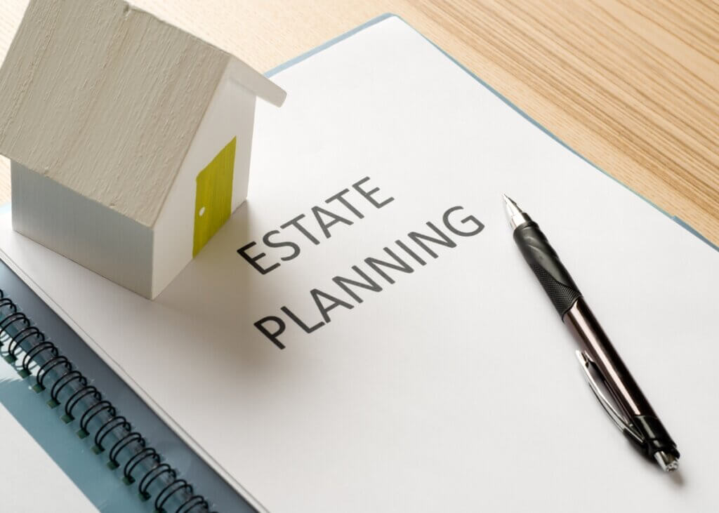 a document on a table titled "estate planning" with a pen on the document and a wood house