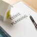 a document on a table titled "estate planning" with a pen on the document and a wood house