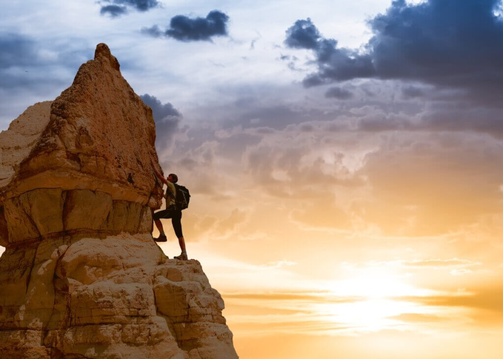 a person climbing to the top of the mountain with the sunset in the back