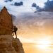 a person climbing to the top of the mountain with the sunset in the back