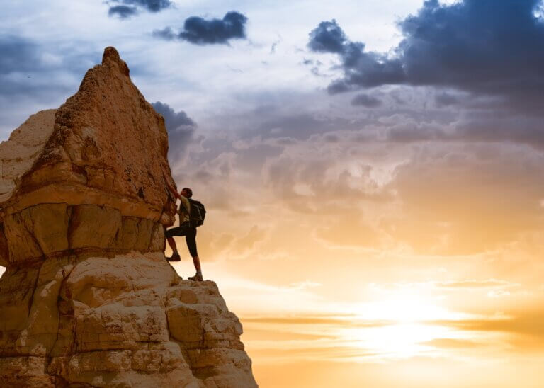 a person climbing to the top of the mountain with the sunset in the back