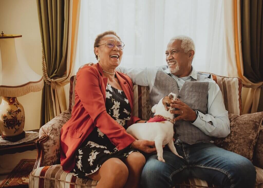 an aging couple sitting on the couch laughing with each other and their dog