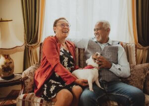 an aging couple sitting on the couch laughing with each other and their dog