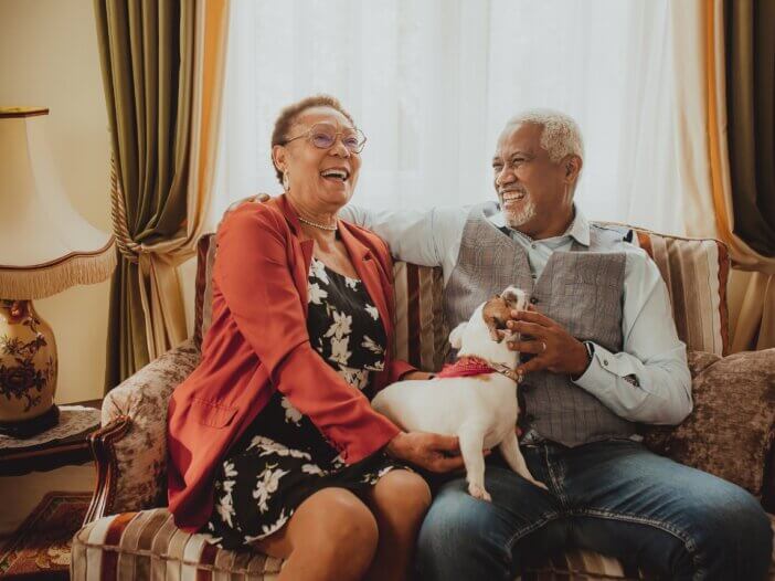 an aging couple sitting on the couch laughing with each other and their dog