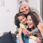 3 generations- a child, their mother, and their grandmother. all on the couch and hugging and laughing each other.