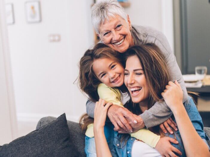 3 generations- a child, their mother, and their grandmother. all on the couch and hugging and laughing each other.