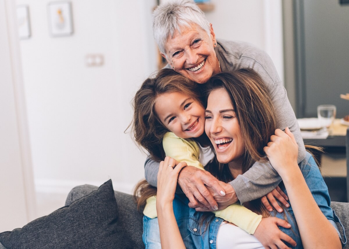3 generations- a child, their mother, and their grandmother. all on the couch and hugging and laughing each other.