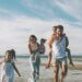 a family at the beach. there are three kids and the two parents with a mom holding one kid and a kid on the dads back.