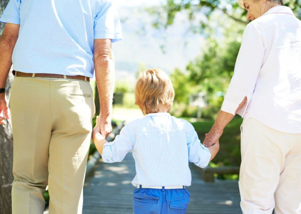 grandparents holding their grandkids hand. a picture from behind and the grandma is smiling at the child