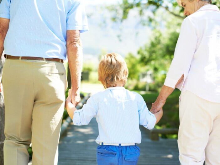 grandparents holding their grandkids hand. a picture from behind and the grandma is smiling at the child