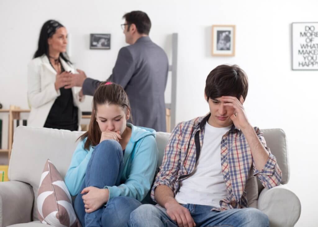 a family fighting. the two parents in the background fighting and the kids sitting on the couch looking frustrated.