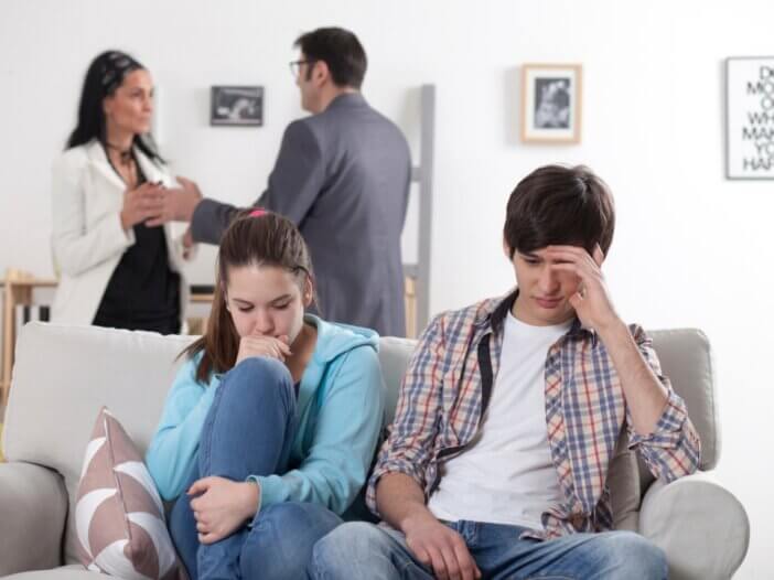 a family fighting. the two parents in the background fighting and the kids sitting on the couch looking frustrated.