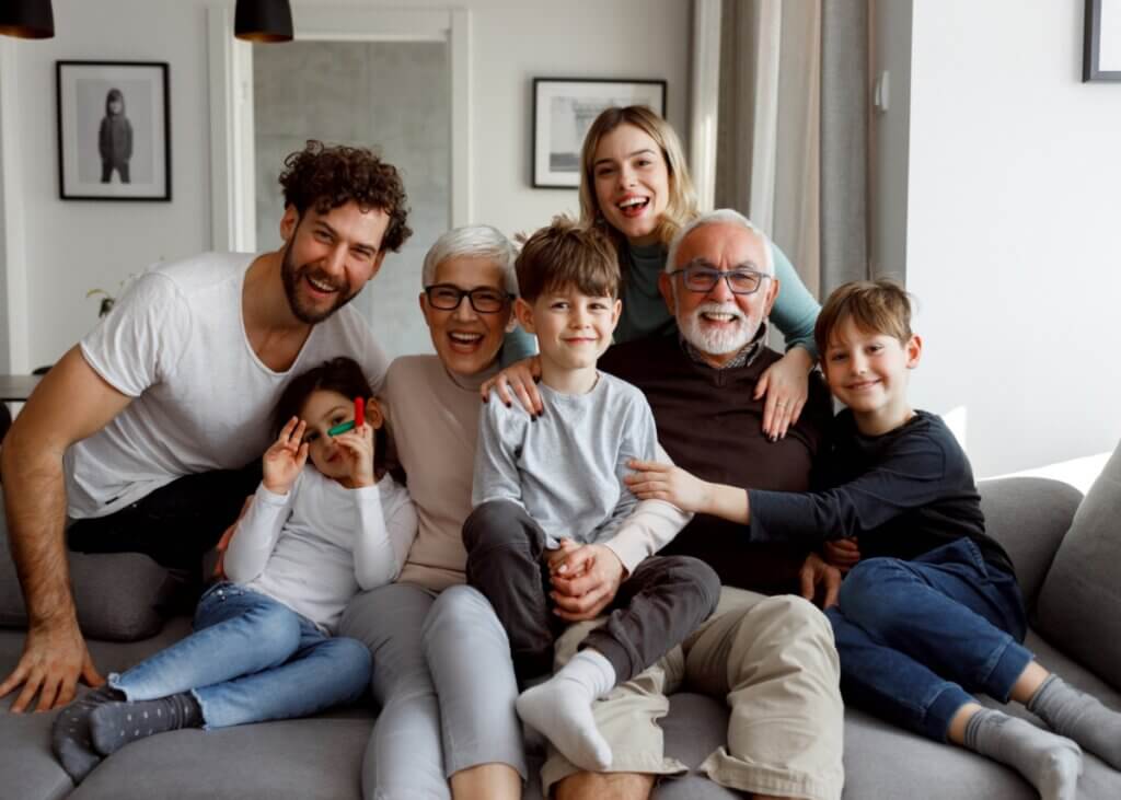 a family sitting on the couch together. a set of grandparents, parents, and three kids