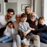 a family sitting on the couch together. a set of grandparents, parents, and three kids
