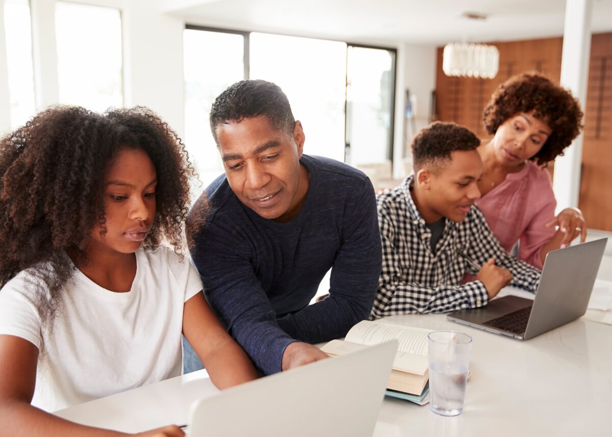 a mom and a dad with their teenage kids sitting on the counter looking at their computers