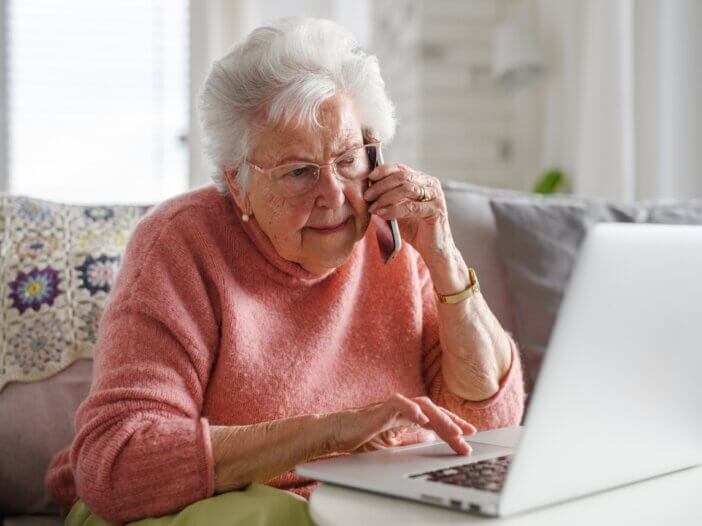 an elderly woman on the phone with someone in front of her computer