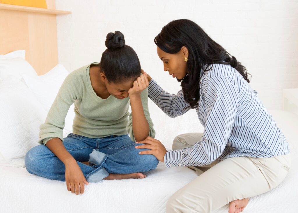 a mom sitting on her couch and consoling her daughter that is crying