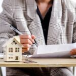 a person reviewing business documents and then there is a model of a house in front of them on their desk