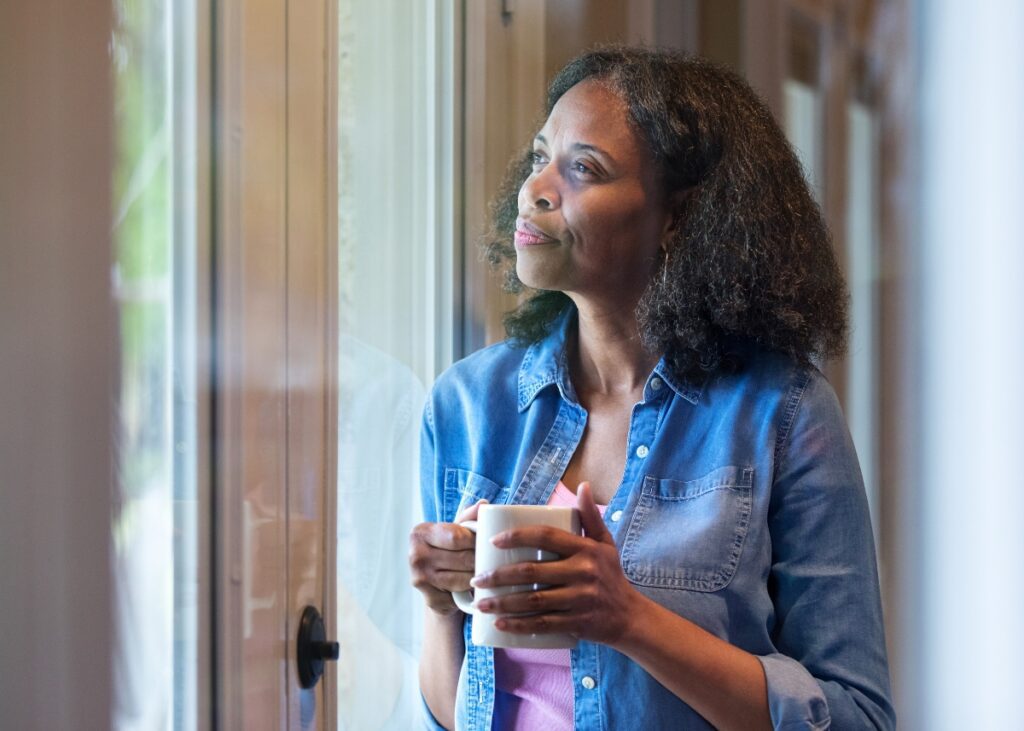 a person holding a cup of coffee looking outside their window reflecting about life.